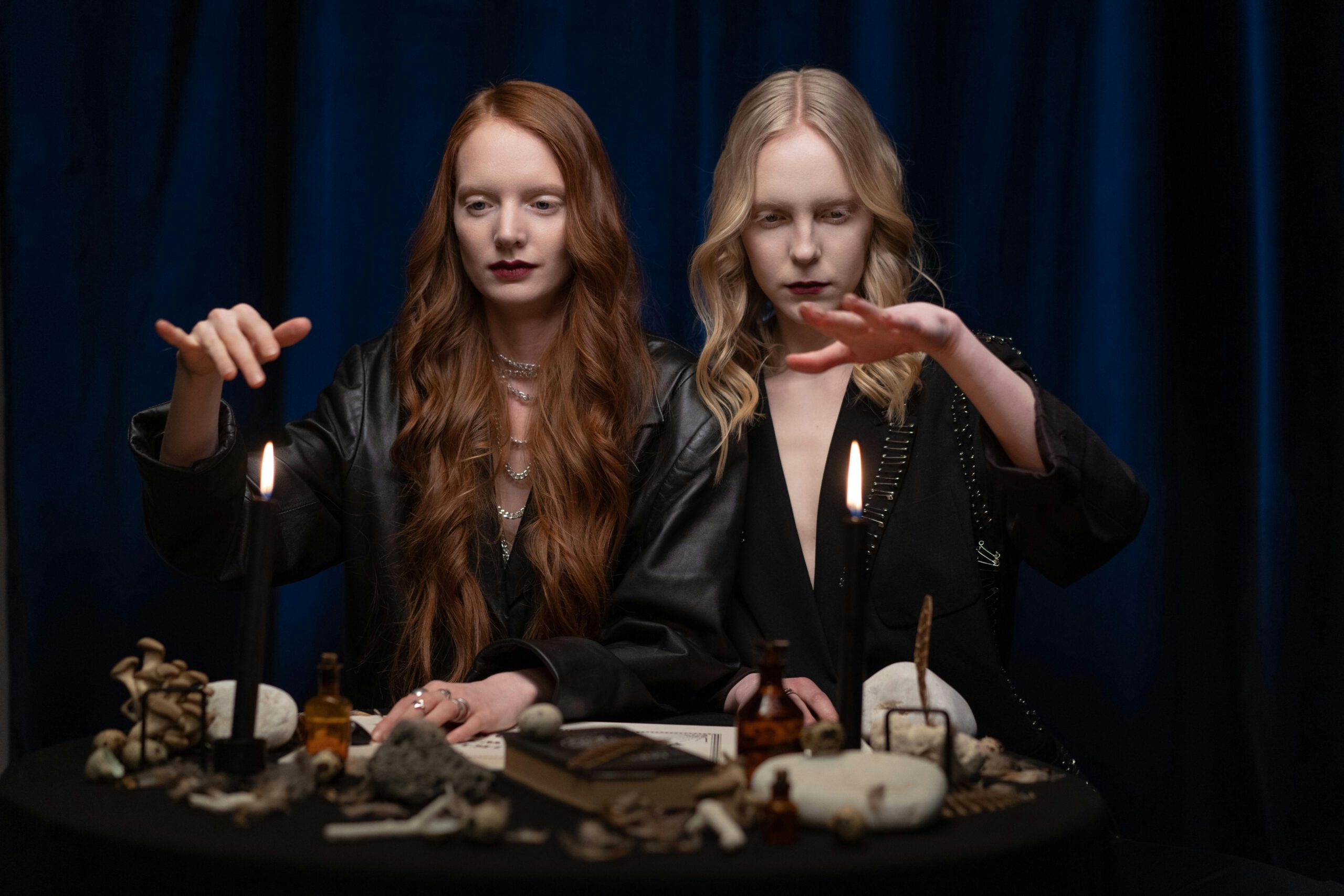 Two women engage in a mysterious candle ritual with stones and artifacts.